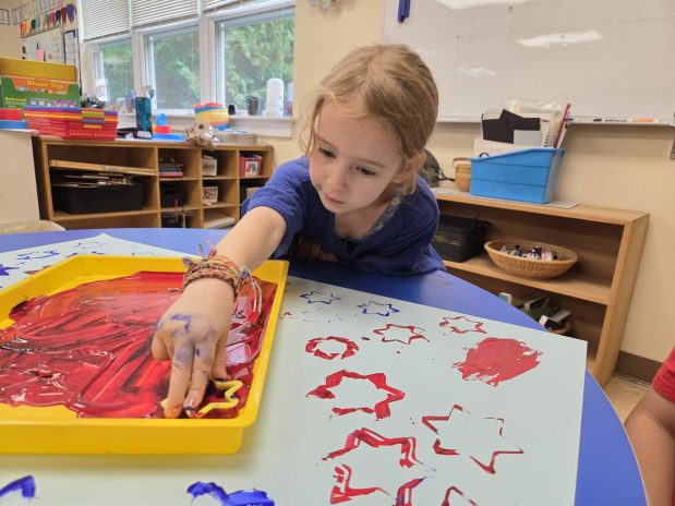 kindergarten student using paint and a stamp to create star art